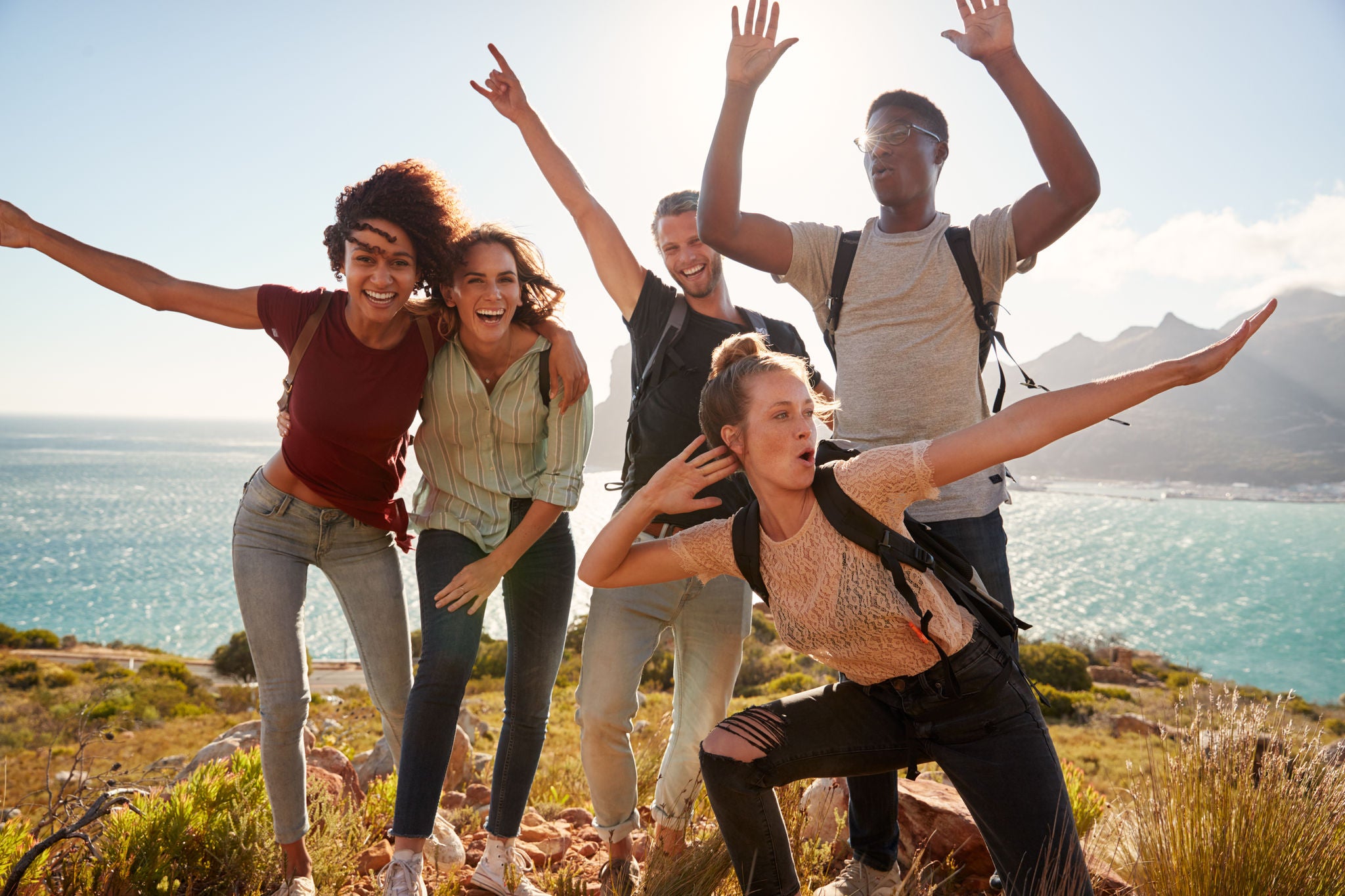 Millennial friends on a hiking trip celebrate reaching the summit and have fun posing for photos