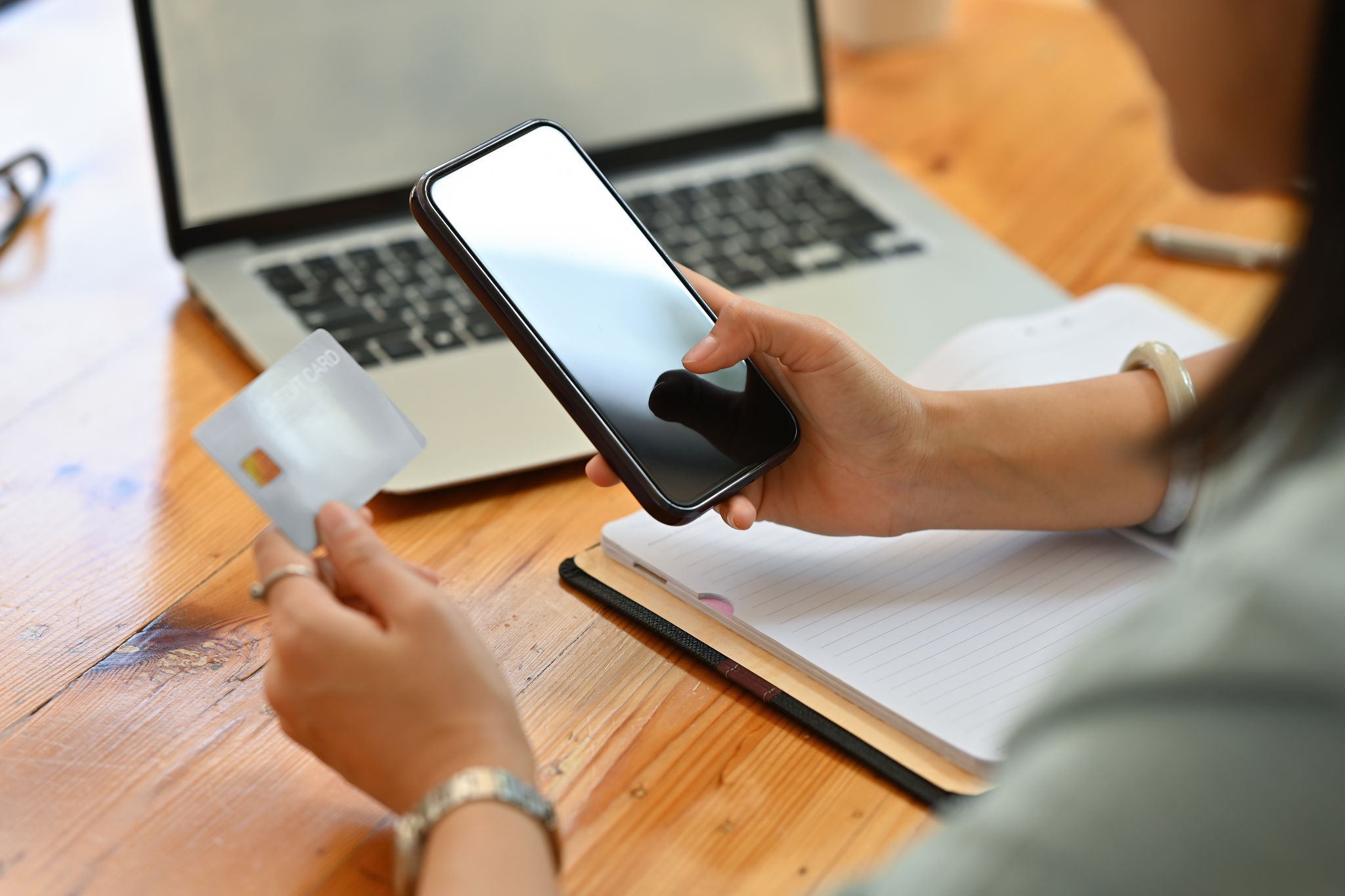 Cropped view of a pretty smiling Asian woman sitting in the office holding a credit card and a smart phone, for finance and technology concept.