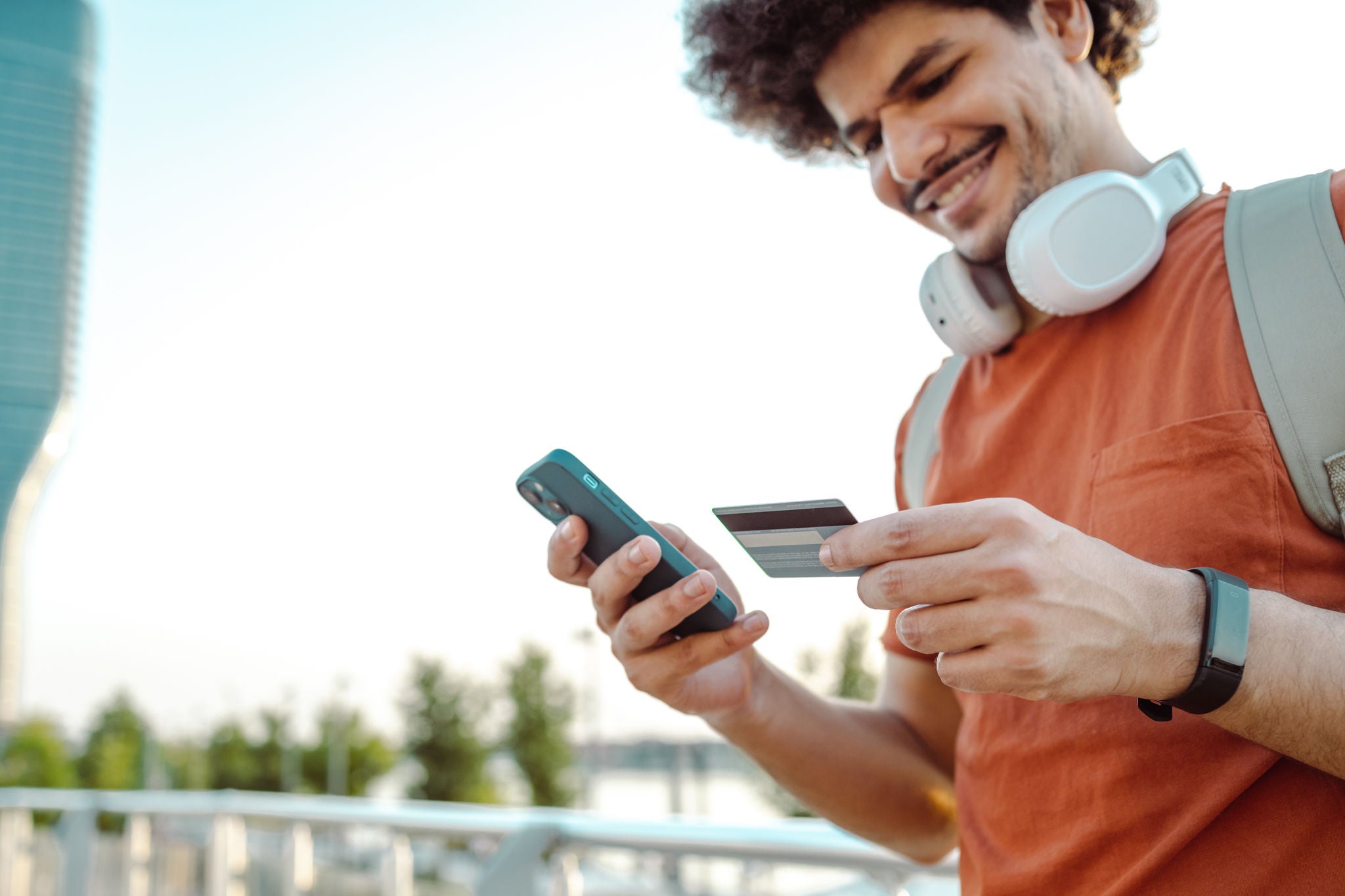 A young smiling man paying easy online. He is using a smart phone and credit card on the go